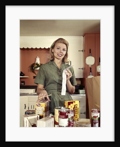 1960s Young Housewife While Checking Grocery Shopping Receipt In Kitchen by Anonymous