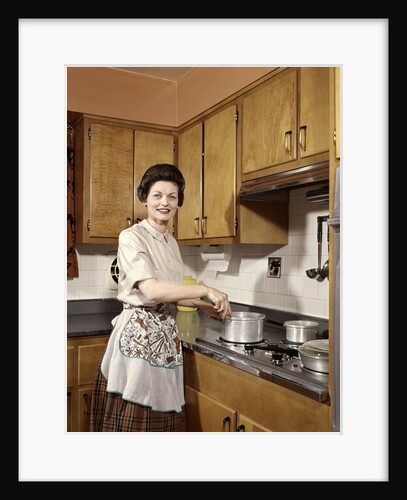 1960s Woman Housewife Wearing An Apron Stirring Cooking Pot At Kitchen Stove by Anonymous