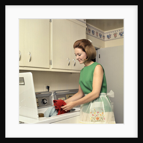 1970s Woman Housewife Homemaker Wearing Apron Loading Laundry Into Washing Machine by Anonymous