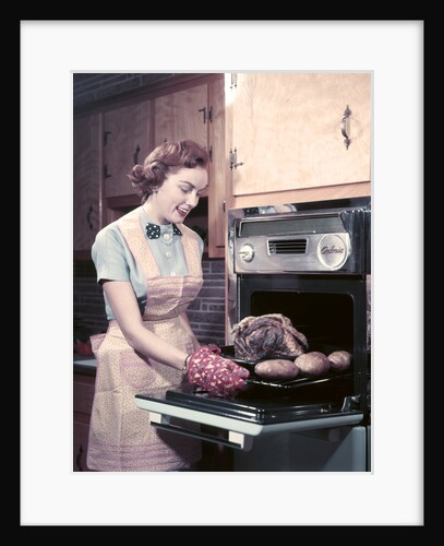 1950s Housewife Wearing Apron And Oven Mitts Taking Roast Beef With Potatoes Out Of Kitchen Oven by Anonymous