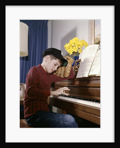 1960s 1970s Impatient Annoyed Looking Boy With Baseball Cap And Glove Practicing Piano Lesson by Anonymous