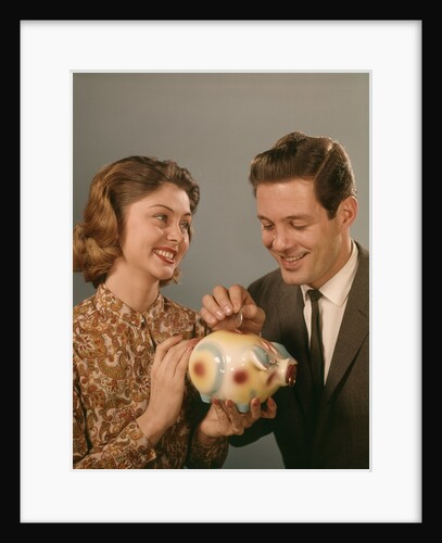 1950s 1960s Happy Couple Man Woman Putting Coins Into Savings Piggy Bank by Anonymous