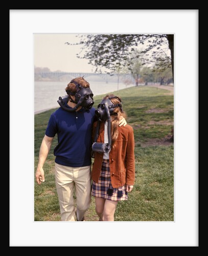 1970s Young Romantic Teenage Couple Man Woman Wearing Gas Masks Walking By River by Anonymous
