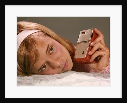 1950s 1960s Teenage Girl Holding Red Silver Small Transistor Radio To Her Ear Listening by Anonymous