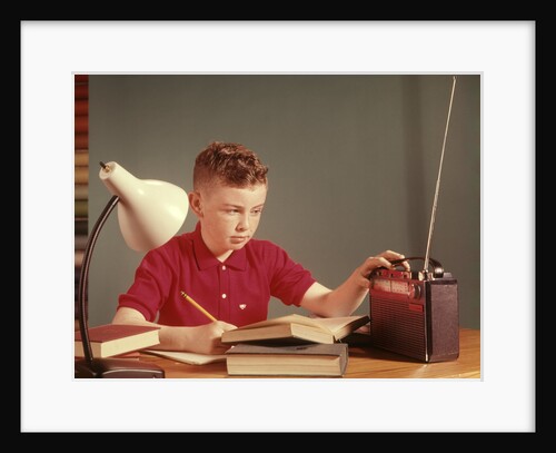 1960s Red Hair Boy Sitting At Deslistening To Portable Radio While Studying Homework by Anonymous