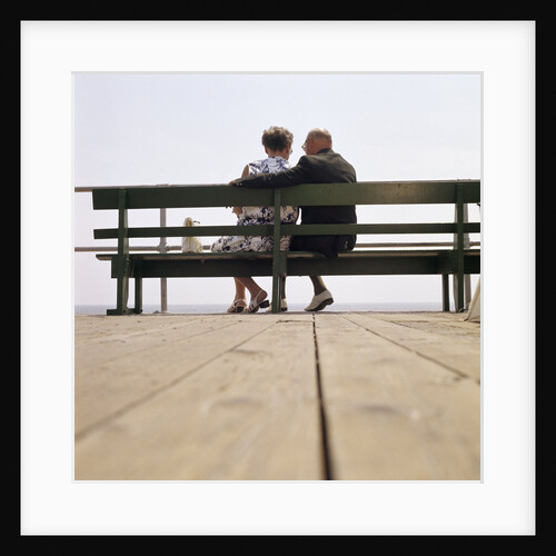 1970s Back View Of Senior Couple Sitting On Boardwalk Bench Overlooking Ocean Beach by Anonymous