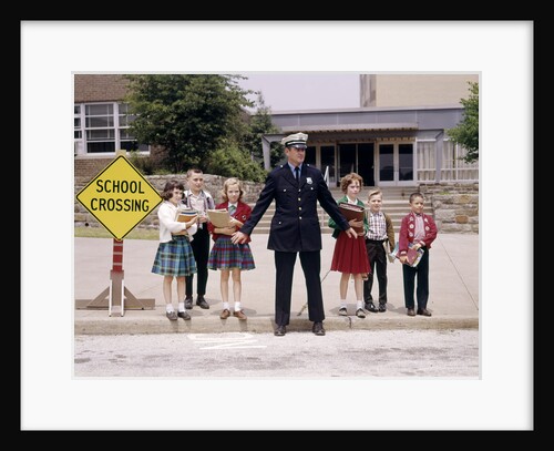 1960s Police Officer Holding Back Elementary School Children Waiting At Curb To Cross Street by Anonymous