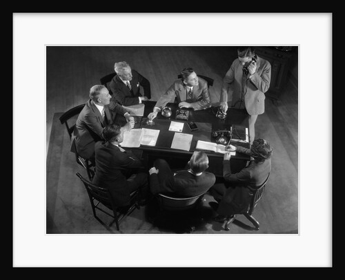 1930s Six Men And One Woman Sitting Around Office Desk While One Man Talks On Telephone by Anonymous