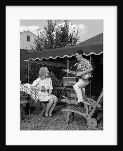 1960s Boy Playing Guitar, Woman Holding Soft Drink Bottle Outside In Backyard by Anonymous
