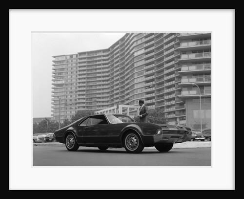 1960s Man In Suit and Hat Standing Beside Oldsmobile Toranado In Front Of Large Apartment Building by Anonymous
