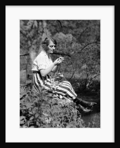 1920s Young Woman In Striped Skirt Sitting On Stream Bank In Woods Braiding Garland Of Wild Flowers by Anonymous
