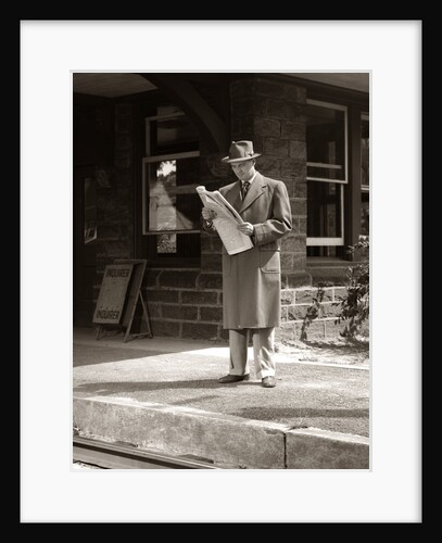 1950s Businessman On Railroad Station Platform Reading Newspaper Waiting For Train by Anonymous
