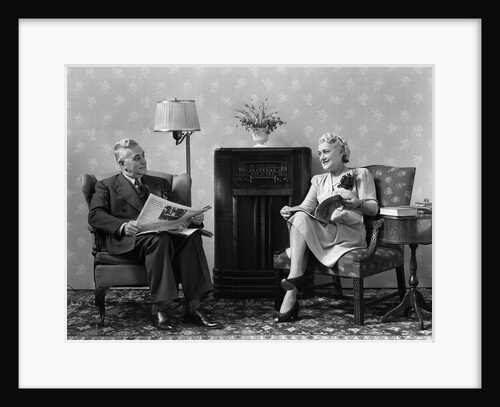 1940s Senior Couple Sitting In Living Room Reading Newspaper And Magazine Listening To Radio by Anonymous