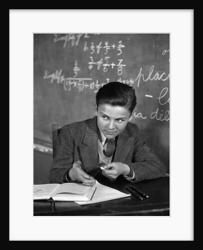 1920s 1930s Boy At Desk In Classroom In Front Of Blackboard Shooting Paper Wad With Rubber Band by Anonymous