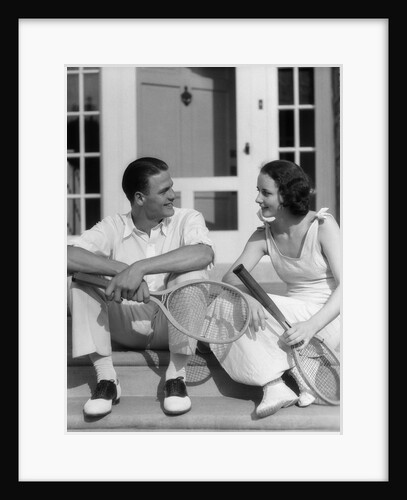 1930s Couple Man Woman In Tennis Whites Holding Racquets Sitting Talking On Steps In Front Of House Outdoor by Anonymous