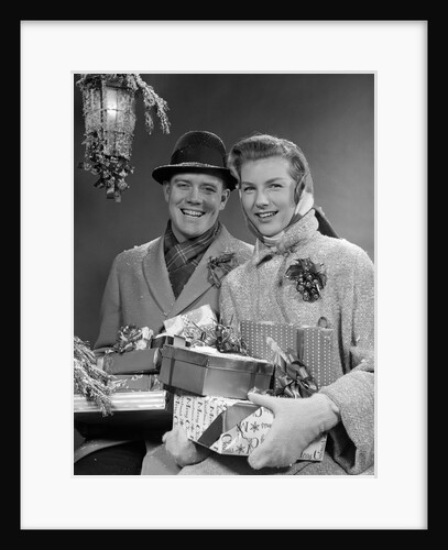 1950s Husband And Wife Carrying Armload Of Christmas Packages Standing In Snow Under Porch Light by Anonymous