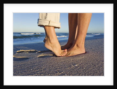 Feet of couple hugging on beach by Anonymous