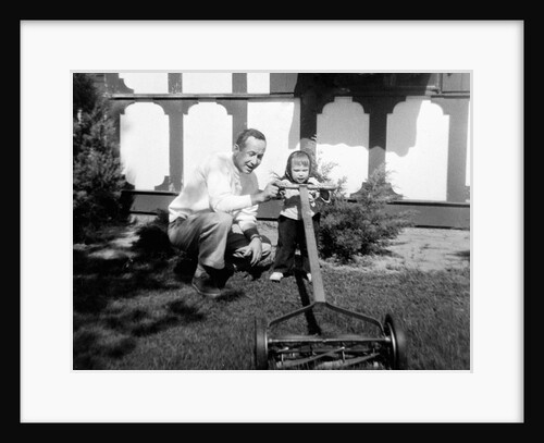 A father show his two year old daughter how to mow the lawn, ca. 1956 by Anonymous