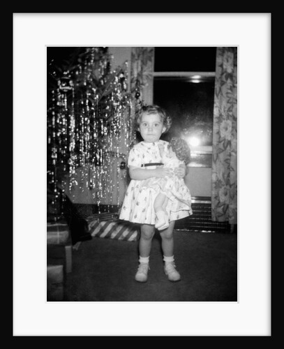 A little girl stands by the Christmas tree clutching her doll, ca. 1955 by Anonymous
