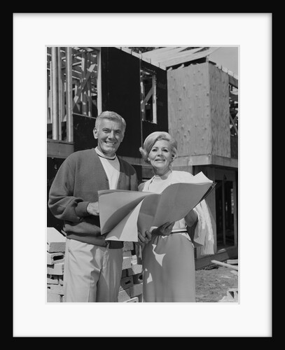 Smiling mature couple holding blueprints on home construction site by Anonymous