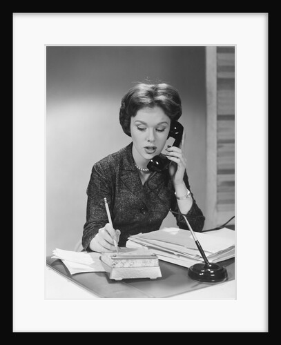 Brunette business woman sitting desk talking telephone writing note on calendar by Anonymous
