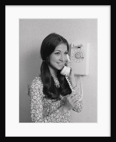 Smiling teenage girl talking on rotary wall telephone by Anonymous