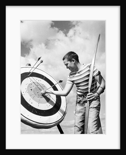 Boy jeans striped t-shirt holding bow & pulling arrow out of target bull's-eye by Anonymous
