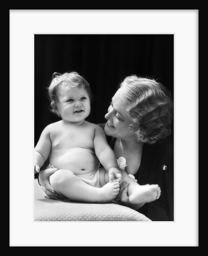 Blond woman mother smiling looking at baby sitting on pillow by Anonymous