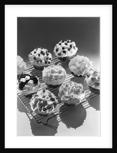 Cupcakes on metal bakers cooling rack decorated with icing sprinkles chips by Anonymous