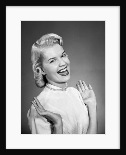 Woman wearing pearls smiling with hands up thumbs tucked under arm by Anonymous