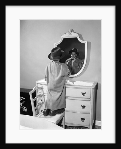 Boy dressed in father's hat coat & shoes standing on chair looking in mirror by Anonymous