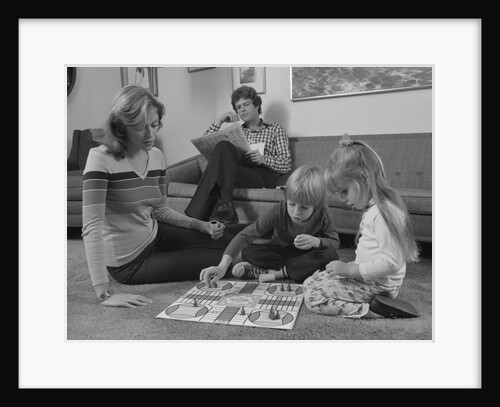 Family mother kids playing board game living room floor father reading newspaper by Anonymous