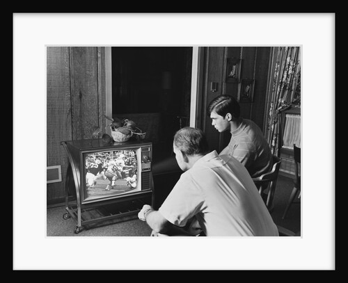 Teen boy watching football game on television with adult dad by Anonymous