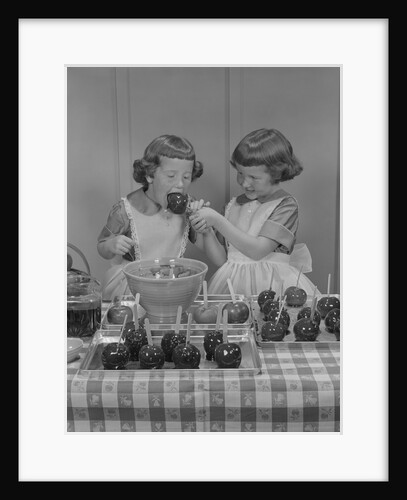 Two twin girls eating making candy apples in kitchen by Anonymous