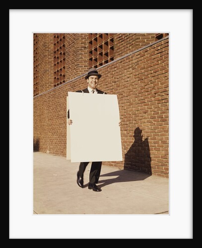 Smiling man wearing suit necktie and hat walking carrying large sandwich board by Anonymous
