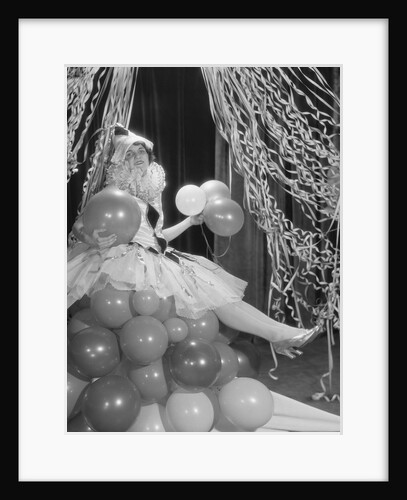 Woman dressed in harlequin costume sitting on stack of balloons by Anonymous