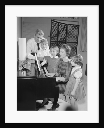 Family standing around piano singing by Anonymous