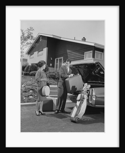 Couple man woman packing luggage into car trunk by suburban house by Anonymous