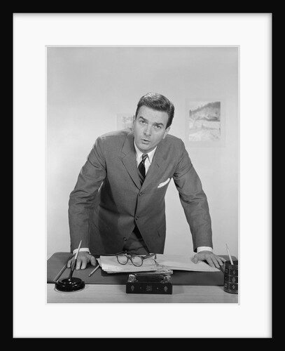 Businessman leaning over desk serious expression looking forward by Anonymous