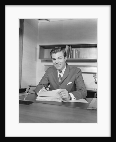 Smiling happy businessman at desk signing papers by Anonymous