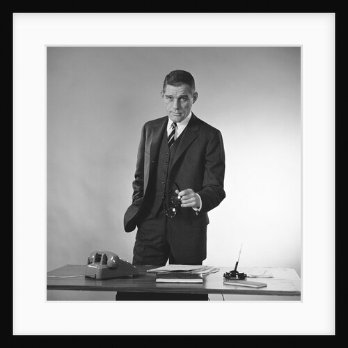 Serious businessman three piece suit standing behind desk gesturing with glasses by Anonymous