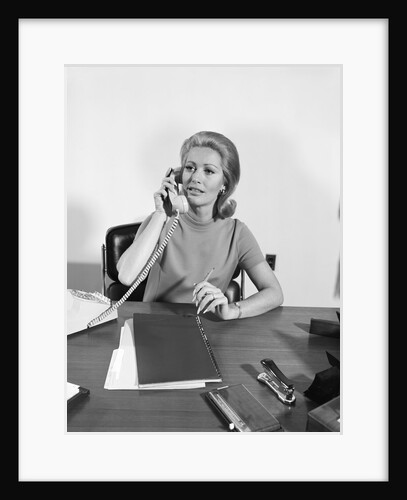 Blond businesswoman talking on telephone sitting at desk by Anonymous