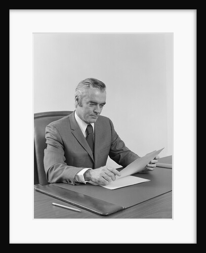 Businessman executive middle aged sitting at desk reading papers by Anonymous