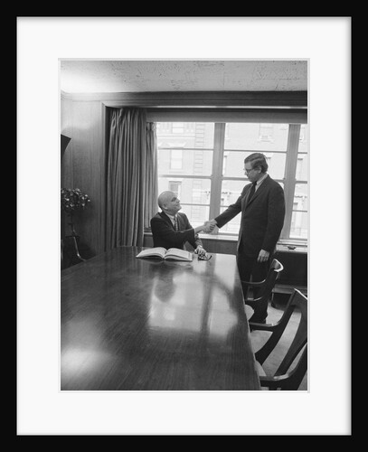 Two men one seated shaking hands long wooden conference table by Anonymous
