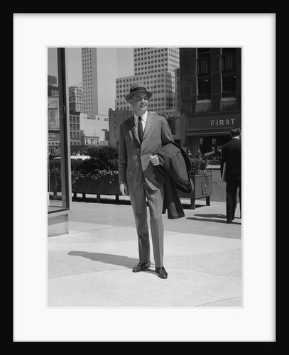 Businessman wearing suit hat carrying top coat standing on city street by Anonymous