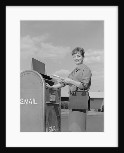 Smiling woman dropping letters in postal mail box by Anonymous