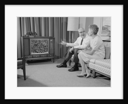 Elderly couple sitting on couch watching television by Anonymous