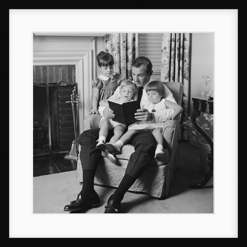 Man father sitting in chair with three children reading book by Anonymous