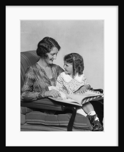 Mother & daughter smiling sitting in chair reading book by Anonymous