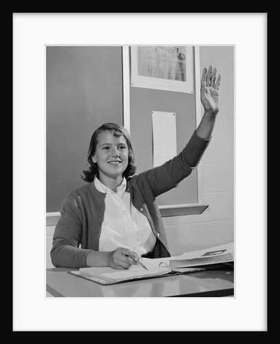 Smiling teen girl sitting classroom desk raising her hand by Anonymous